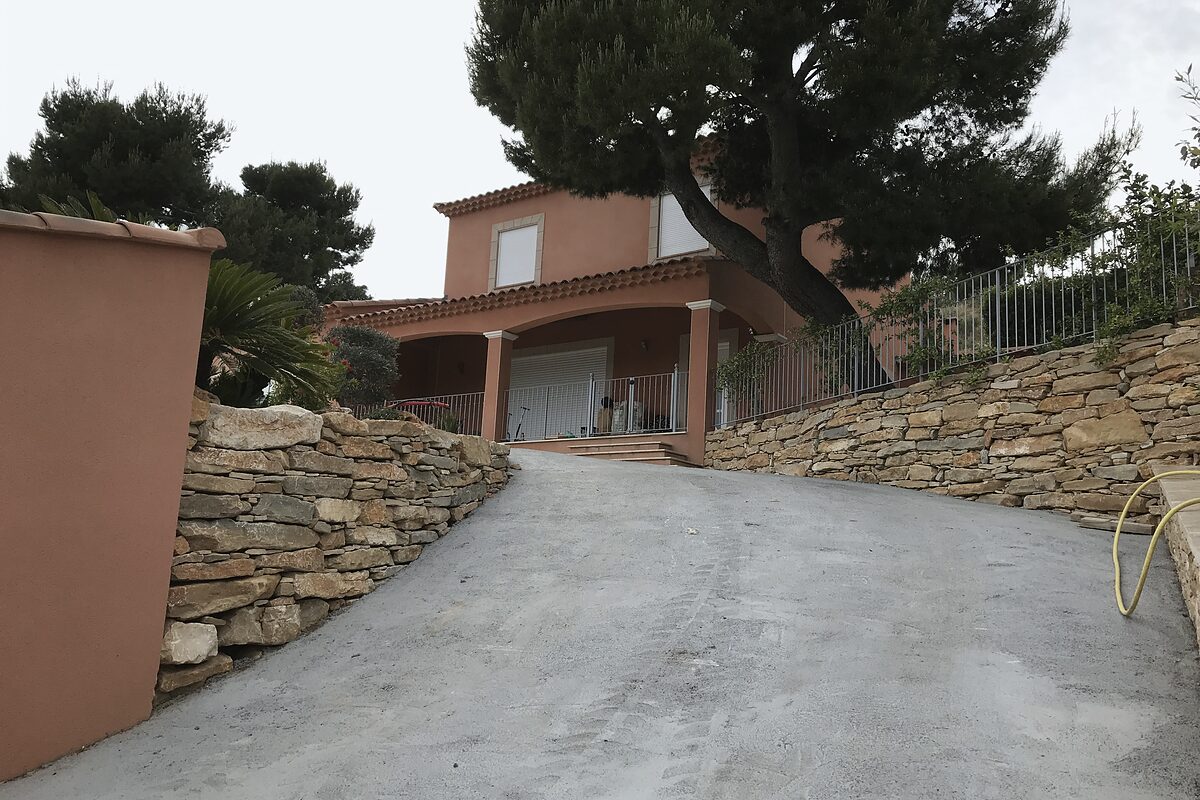 Allée bordée d'un long mur en pierres devant une villa